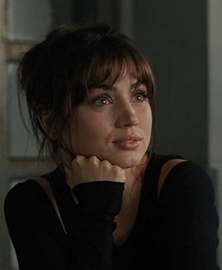 A close-up portrait of a woman with dark hair and bangs, resting her chin on her hand, looking upward with a thoughtful expression.