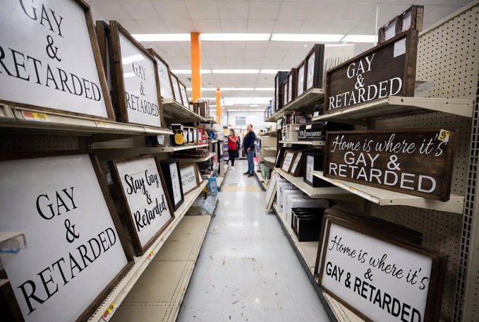 A store aisle displaying multiple wooden signs with the phrases 'GAY & RETARDED' and 'Home is where it's GAY & RETARDED' on shelves.