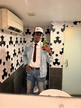 A man wearing a white "RedotsClub" cap, denim jacket, white shirt, and black tie takes a mirror selfie while holding a green phone, posing in a bathroom with geometric black-and-white tiled walls. The image ties to the post's celebration of the RedotsClub Mixer at Unchain Summer, with the cap displaying the club's branding.