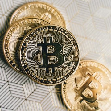 A close-up photograph of physical Bitcoin tokens stacked on top of dollar bills.