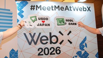 A promotional photo from WebX 2026 featuring the hashtag '#MeetMeAtWebX' with two people holding props for 'USDD JAPAN' and 'HODL & EARN'.