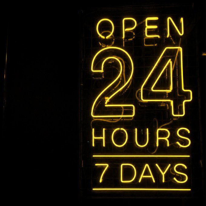 A glowing yellow neon sign against a black background reads "OPEN 24 HOURS 7 DAYS," visually reinforcing the "24/7" message by highlighting continuous, around-the-clock availability.