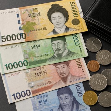 South Korean won banknotes in denominations of 50,000, 10,000, and 1,000 won are displayed alongside Korean coins, visually representing the currency discussed in the news about the won's slight gain against the US dollar as it begins 24-hour trading.