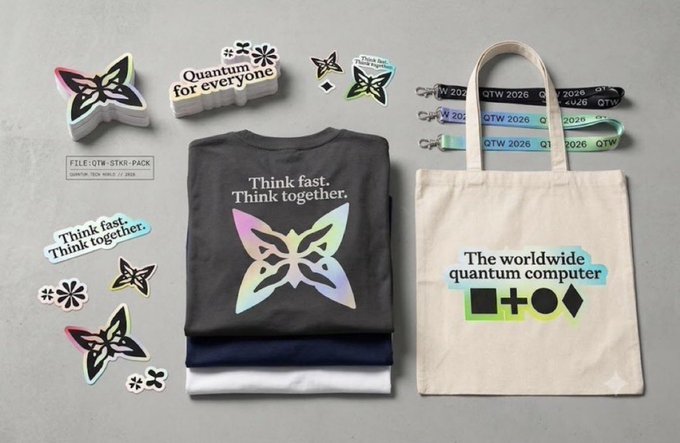 A flat-lay photograph of 'Quantum for everyone' merchandise, including a black t-shirt with a butterfly graphic reading 'Think fast. Think together.', a beige tote bag stating 'The worldwide quantum computer', stickers, rubber stamps, and lanyards labeled 'QTW 2026'.