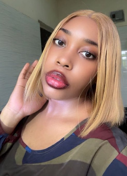 A close-up selfie of a young woman with blonde hair posing with her hand near her face.