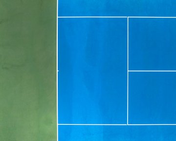 A bird's-eye view of a blue tennis or pickleball court next to a green court, divided by white boundary lines.