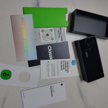 An unboxing flat-lay displays tech accessories including holographic cards, a QR code card, and a green paper holder arranged on a white surface.