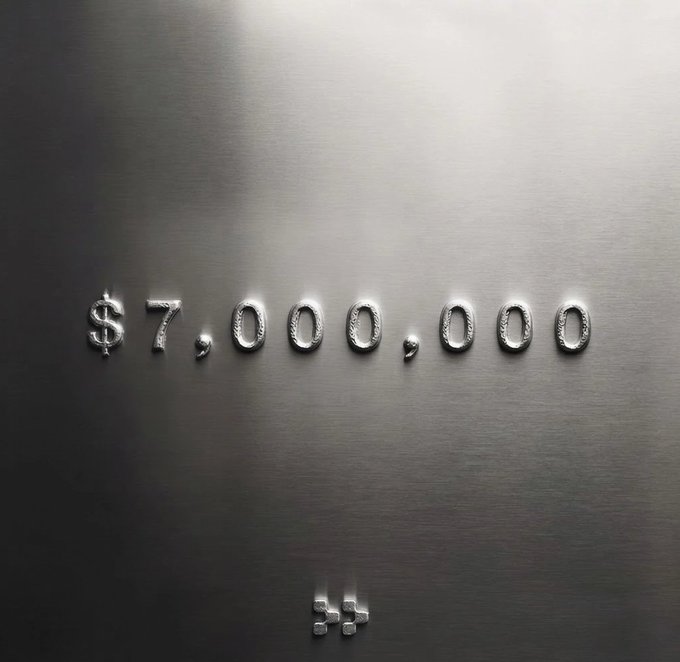 A dark, metallic textured image displaying '$7,000,000' in embossed silver text with a small logo below.