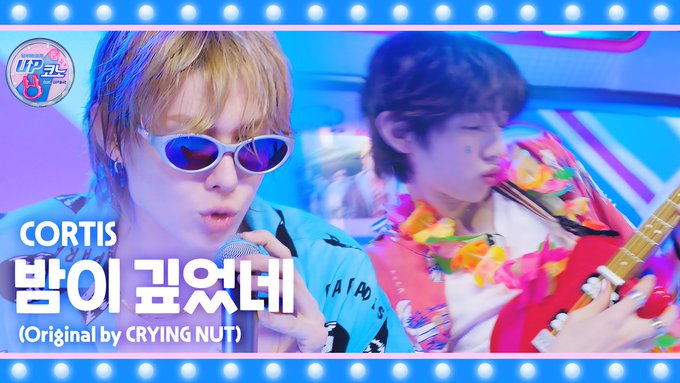 A promotional thumbnail for "UP코노 EP.16" features K-pop group CORTIS (코르티스) performing their cover of "밤이 깊었네" (originally by CRYING NUT), showing two members—one wearing blue sunglasses and singing into a microphone, and another playing a red electric guitar—against a vibrant blue stage backdrop.