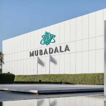The exterior of a white modern building displaying the 'MUBADALA' company logo in dark lettering with its teal emblem above.
