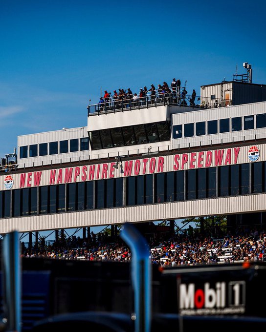 An exterior view of the grandstands at New Hampshire Motor Speedway, showing spectators on the upper balcony and a Mobil 1 sign in the foreground.