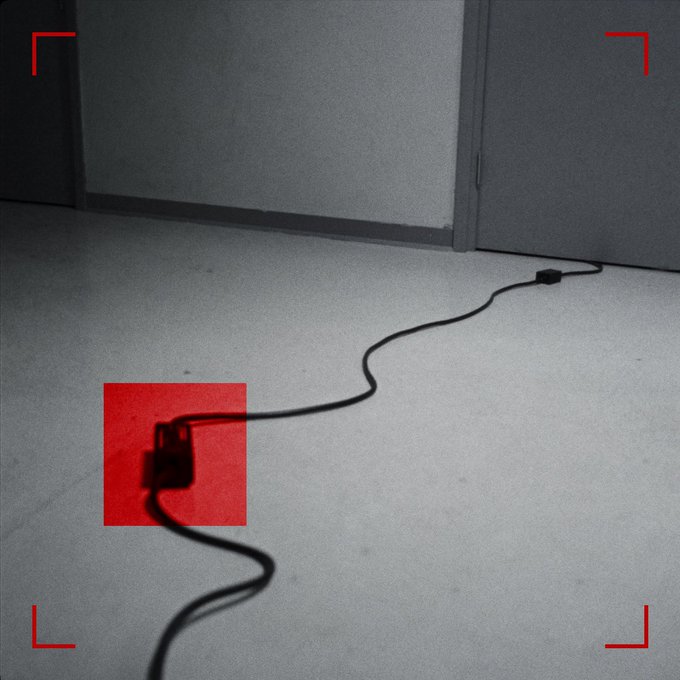 The image appears to be a black-and-white surveillance-style shot with red framing brackets in the corners, showing a power cable snaking across a concrete floor near a doorway, with a red highlight box emphasizing a plug/junction point in the lower-left area. Fitting the caption "GM everyone / Any signs you see?"—the highlighted cable and plug serve as a subtle visual clue, suggesting the poster is playfully prompting viewers to look for hidden signs or "hooks" like this one.