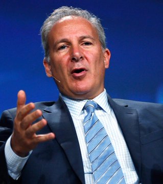 A middle-aged man with grey hair, wearing a dark suit and a blue striped tie, gestures with his hand while speaking, appearing to be giving a presentation or interview.