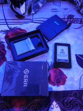 A beautifully unboxed ERA E-Reader Kit, complete with a black sleeve, charging cable, and boxed device, rests on a floral-patterned surface. The post celebrates welcoming @LoSyohana819 into the ERA family, and the image shows the very kit that made their day.
