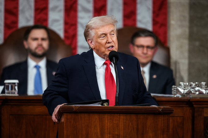 President Trump speaks at a podium in front of an American flag backdrop, likely during a speech or address, as he personally takes charge of the CLARITY Act. The image relates to the post by showing a figurehead advocating for the bill's passage.