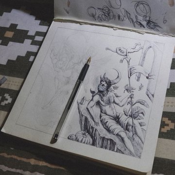 A sketchbook lies open on a patterned textile, displaying a detailed pencil drawing of a horned figure sitting on rocks with a small ghost-like companion on a staff, alongside a mechanical pencil.