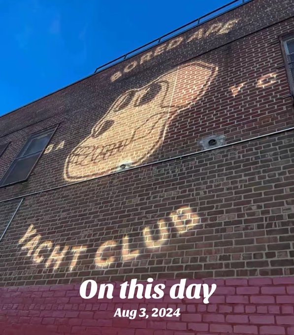 A brick building wall features a projected shadow artwork of a character with text reading 'LIGHT A WISH' and an overlay stating 'On this day Aug 3, 2024'.