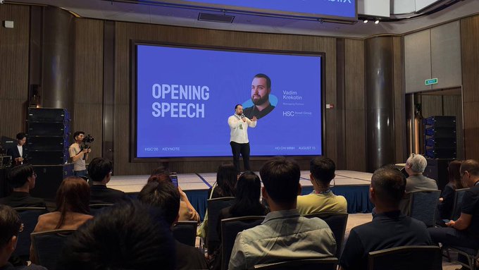 A conference opening speech with Vadim Krikun of HSC Head Group, where a presenter stands on stage in front of a large screen displaying his name and the HSBC Sri Lanka logo while the audience watches.