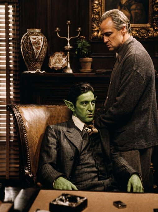 A green-skinned elf-like man in a pinstripe suit sits in a leather chair while a gray-haired man in a sweater places a hand on his shoulder in a richly appointed study, echoing the mafia warning "Never go against the family" by depicting a tense moment of counsel or control within an organization.