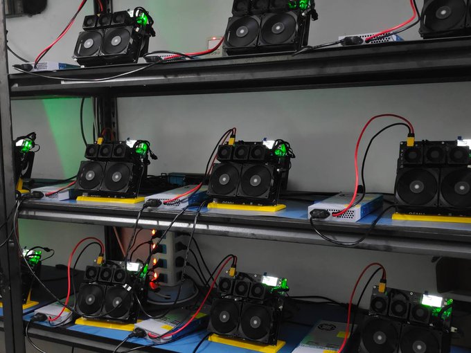 Multiple BSB NerdOctaxe cryptocurrency mining rigs are stacked on metal shelving, each equipped with cooling fans and indicator lights, with a tangle of power and data cables connecting the units together.