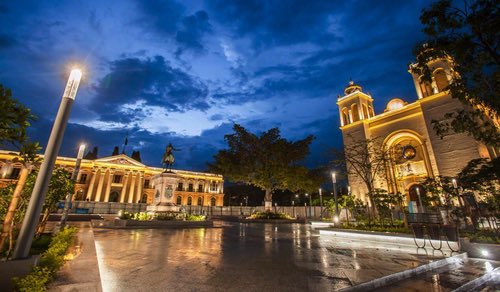 An illuminated grand plaza at dusk, framed by classical architecture and a statue on a pedestal under a deep blue twilight sky, evokes a timeless civic grandeur. The caption "Bitcoin Country" ties this majestic scene to the post's vision of a sovereign, philosophical society built around Bitcoin, suggesting Bitcoin as the cornerstone of a refined and purposeful civilization.