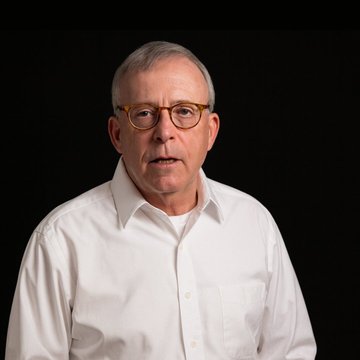 Peter Brandt, a renowned trading analyst, speaks against a black background while wearing a white shirt and glasses, accompanying an insight about his views on Bitcoin outperforming AI stocks over the next two to three years.
