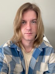 A portrait of a person with shoulder-length blonde hair wearing a blue and white plaid flannel shirt over a yellow t-shirt.