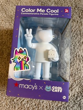 A boxed 'Color Me Cool' commemorative figurine by Macy's x Cool Cats, featuring a blank white figure holding a cat mask and making a peace sign.