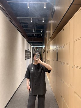 A person in a black t-shirt and sunglasses takes a mirror selfie in a hallway lined with wooden lockers, possibly at a gym or fitness facility, reflecting their post-workout glow referenced in the caption about finding happiness through exercise and feeling "rebooted" after a good sweat session.