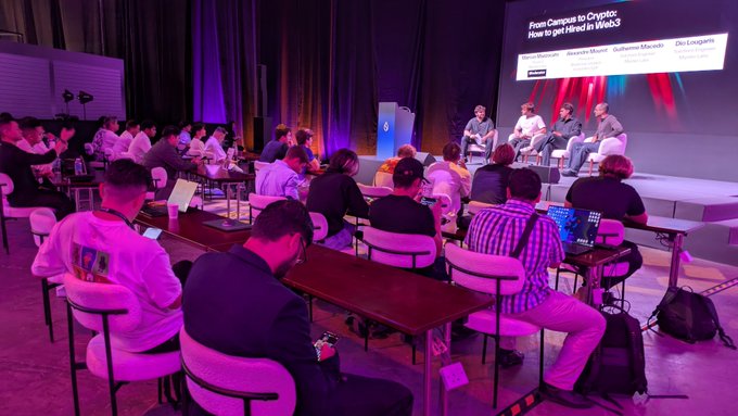 A panel discussion titled 'From Campus to Crypto: How to get Hired in Web3' with moderators Bruno Mauser, Guillaume Massol, and Jia Lingng, shown on a stage screen while attendees watch from tables below.