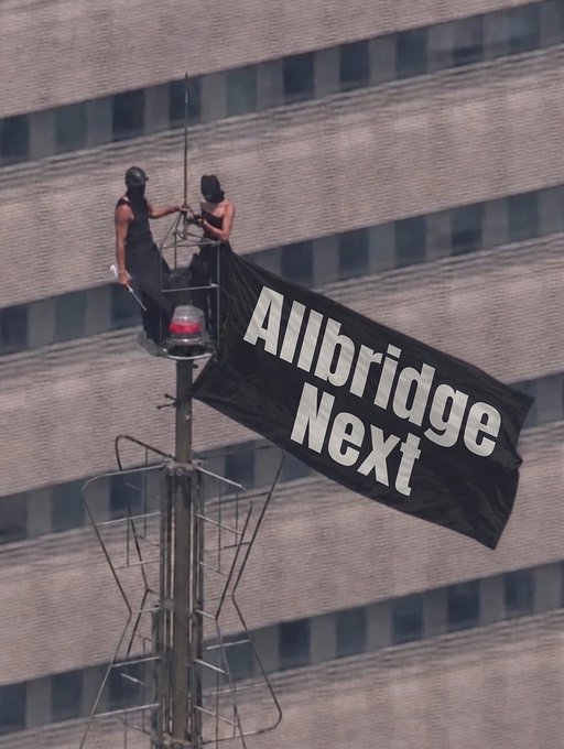 Two people perched atop a tower unfurl a black banner reading "Allbridge Next," visually promoting the @Allbridge_io protocol while the caption highlights how the project maintains ongoing security measures like active bug bounties rather than relying solely on past audits.