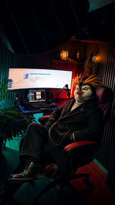 An anthropomorphic penguin with orange spiky hair sits in a red office chair in a moody trading setup, with dual monitors displaying candlestick charts and a studio light overhead.