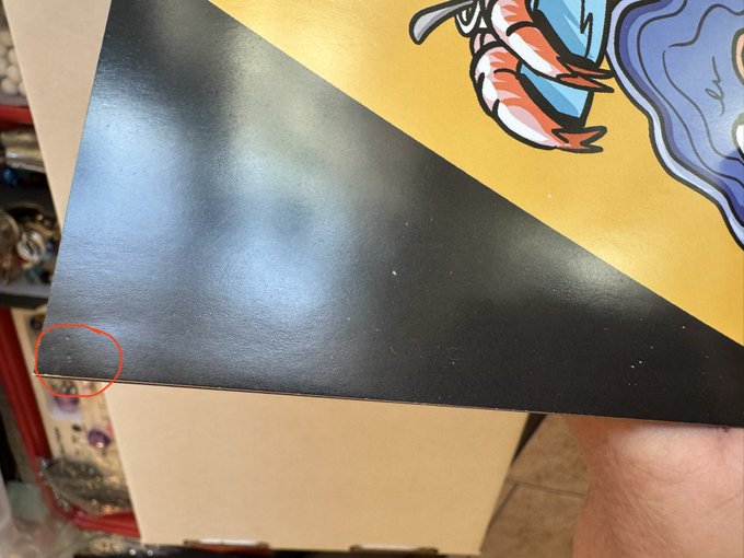A photo of a black poster or board with a red circle drawn around a small defect or tear in the corner.