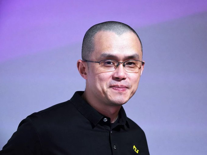 The image features a man wearing glasses with a black shirt against a purple background. The man has short hair and appears to be smiling at the camera. There are no texts or other objects present in the image, so we can only see the man's face and his attire.