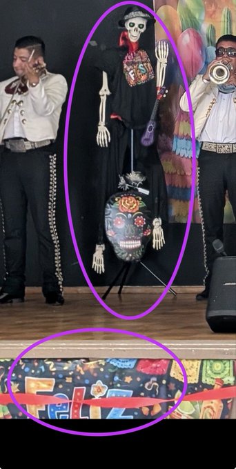 A Day of the Dead display features a skeleton figure and a decorated skull with purple circles highlighting these elements, with mariachi musicians visible in the background.