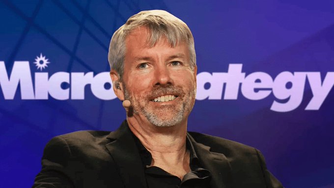 A man with gray hair and beard smiling in front of a 'MicroStrategy' branded backdrop.