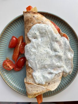 A folded tortilla wrap generously topped with creamy herb sauce, served on a blue ceramic plate alongside halved cherry tomatoes. The image ties into the post's playful SPF metaphor by presenting a "summer food" pairing—likely referencing Fhenix's data-protection messaging through the visual of a sun-weathered meal.