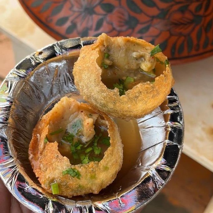 Two golden fried bread cups (pani puri/golgappa) filled with potato mixture, chickpea curry, and garnished with cilantro, served in a silver bowl.