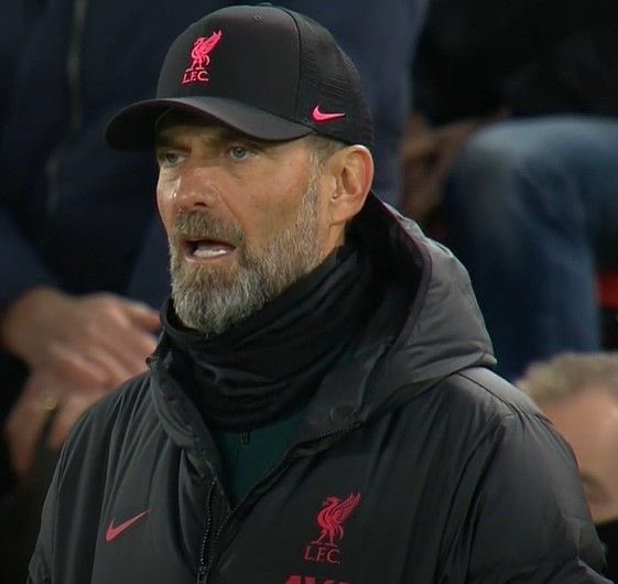 Liverpool FC manager Jürgen Klopp, identifiable by his LFC cap and jacket, looks on with a serious expression during a match.