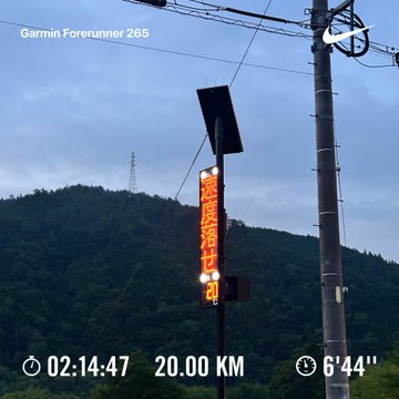 A Garmin Forerunner 265 watch face overlay shows a 20.00 KM run completed in 02:14:47 with a 6'44" pace, set against a dusk sky with mountains and a vertical LED sign in Japanese.
