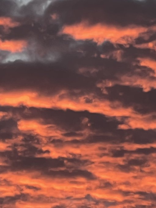 A dramatic sunset or sunrise sky filled with dark, horizontal cloud formations illuminated in vivid orange and red hues.