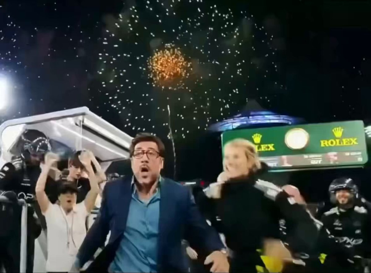 ers,sui,andtherolex are the main characters in the image. They're seen standing near a watch with fireworks going off in the background as well. The picture seems to be related to the fact that Sui was just promoted and reached $100+ this year at the Rolex factory, which is described in the caption provided. This photo captures an exciting moment during the celebration or ceremony when the fireworks are happening while they're surrounded by a crowd of people watching the event unfold.