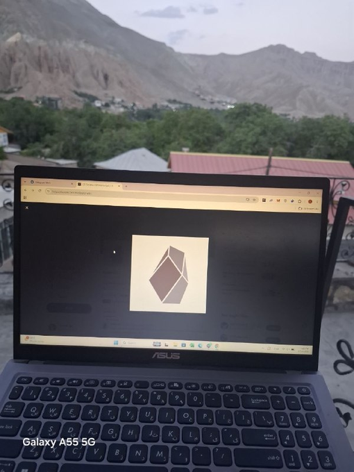 An ASUS laptop sits outdoors with a mountainous landscape in the background, its screen displaying a web browser with a geometric logo, watermarked 'Galaxy A55 5G'.