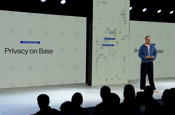 The image shows a man standing at a podium with a microphone, giving a speech or presentation. The background features two large screens displaying information related to privacy and security for transactions. The text "PRIVACY ON BASE" can be seen on both screens, indicating that this is an event focused on privacy and security in the context of financial transactions.