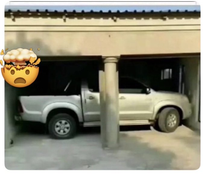 A silver pickup truck parked in a garage, appearing to have crashed into or be stuck against a central pillar, with a shocked face emoji overlaid on the left.
