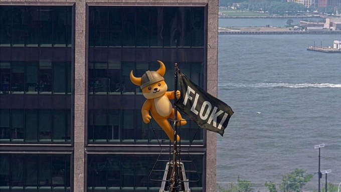 A cartoon dog mascot wearing a Viking helmet holds a black flag reading "FLOKI" while perched atop a building overlooking a body of water, aligning with the "JOIN THE MOVEMENT @FLOKI" call to action.