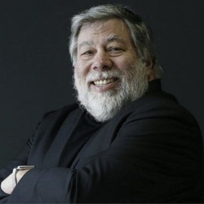 A portrait of a smiling older man with a gray beard wearing a black shirt against a dark background.