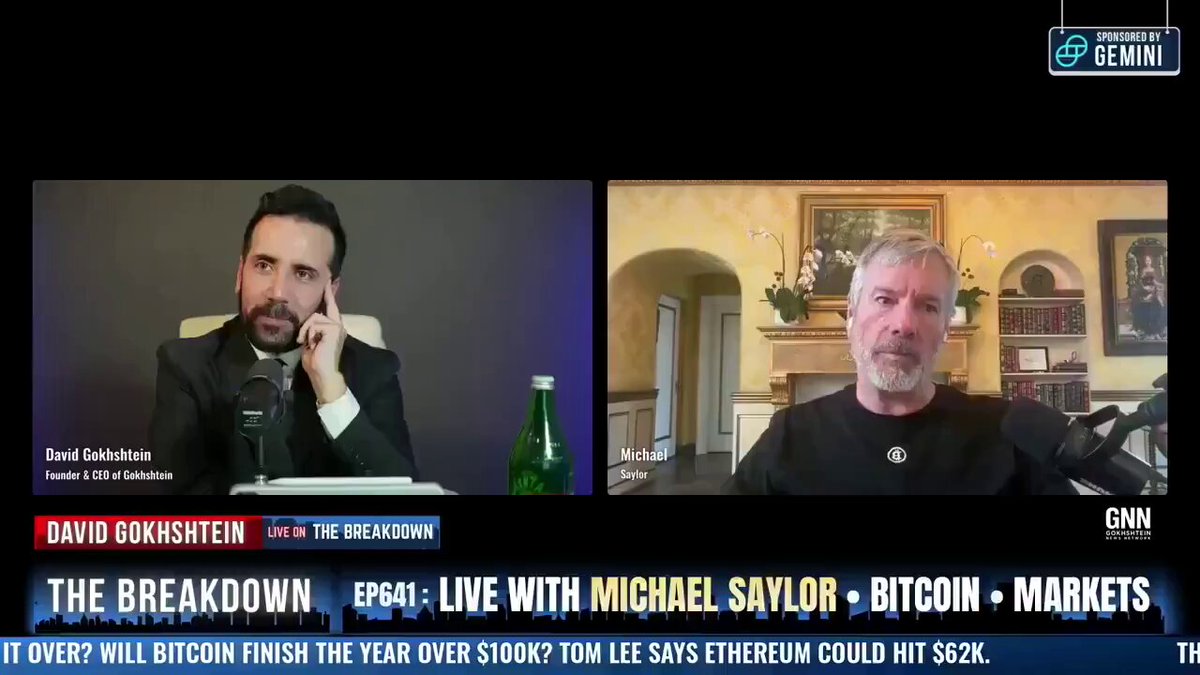 The image shows a conversation between two men sitting at a table with a bottle of beer next to them. They are discussing the breakdown of Bitcoin, which has been featured in an article about cryptocurrency strategies. One man is talking while the other listens attentively. The scene suggests that they might be discussing the implications and potential outcomes of the breakdown of Bitcoin on the market.