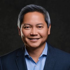 A professional headshot shows a smiling middle-aged man with gray hair wearing a dark blazer over a light blue shirt against a dark background, likely representing Strategy CEO Phong Le as referenced in the accompanying post about his comments on AI and Bitcoin.