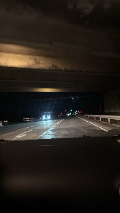 The image shows a view from inside a car driving through a tunnel at night, with bright headlights from oncoming traffic visible ahead. No visible text, numbers, tickers, or names appear in the image; the "$ANSEM" reference in the post seems unrelated to the nighttime driving scene captured here.